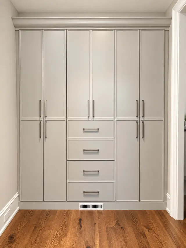 Light gray built-in wardrobe with tall doors, brushed nickel pulls and a four-drawer center stack
