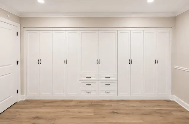 Long wall of white shaker built-in wardrobes with black pulls and six center drawers