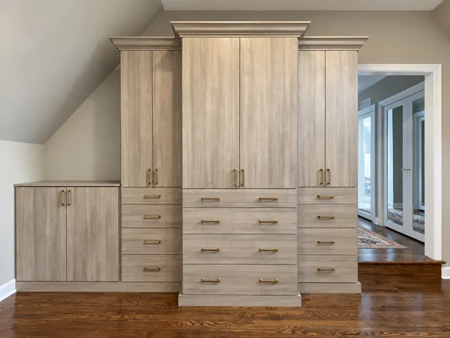 Gray wood-grain wardrobe with crown molding, tall cabinets and drawers, beside a low cabinet under a sloped ceiling