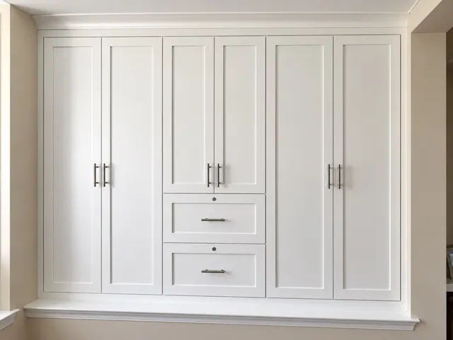 White shaker built-in wardrobe set into a wall niche, with tall doors, brushed nickel pulls and two center drawers