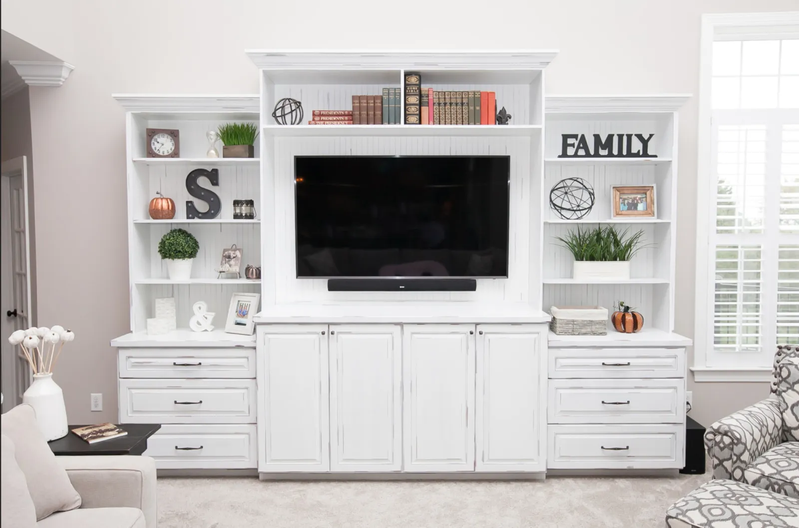 White entertainment center with a wall-mounted TV and soundbar, flanking open shelves, base cabinets and drawers
