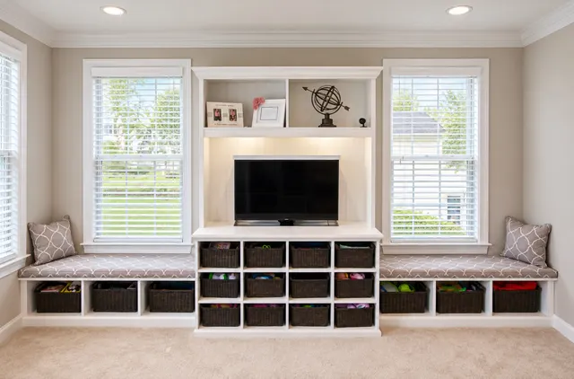 White TV unit with lit beadboard back, cubbies with wicker baskets, and cushioned window seats on both sides