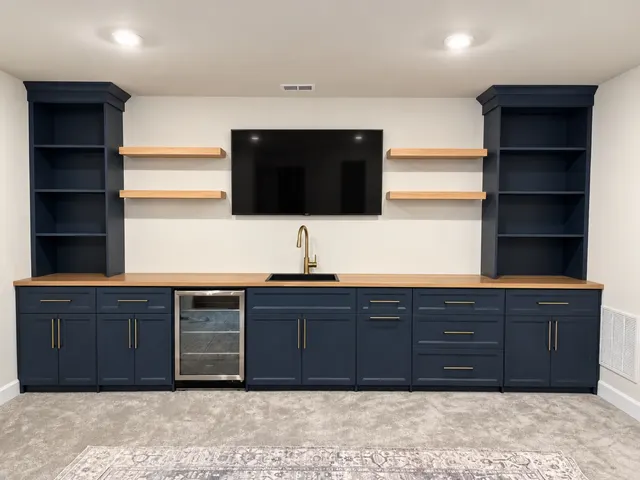 Navy basement bar wall with open bookcases, wood floating shelves, a butcher block counter, sink and wine fridge