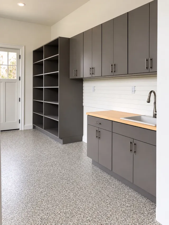 Gray garage open shelving unit and wall cabinets over a butcher block counter with a sink, near a side door