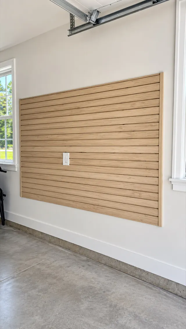 Wood-look slatwall panel mounted on a garage wall between two windows, above a concrete floor