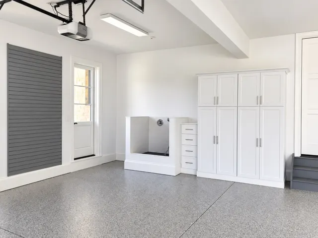 Garage with gray slatwall, a white tiled dog wash station, a drawer stack and tall white cabinets