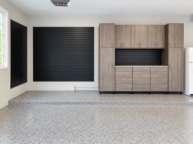 Gray wood-grain garage cabinets around a drawer bank, with black slatwall panels on a speckled epoxy floor