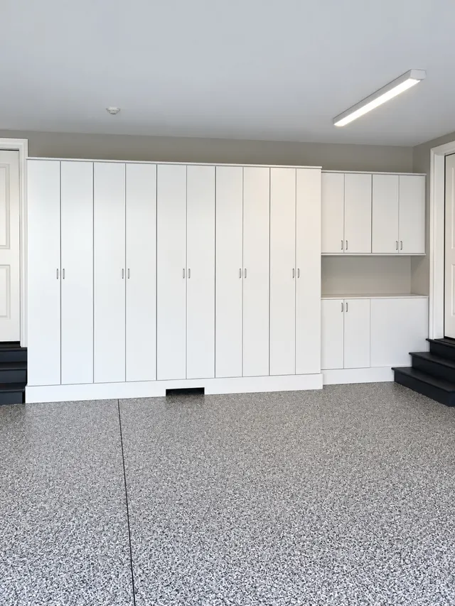 Wall of white garage cabinets with tall doors and a counter section on a speckled epoxy floor