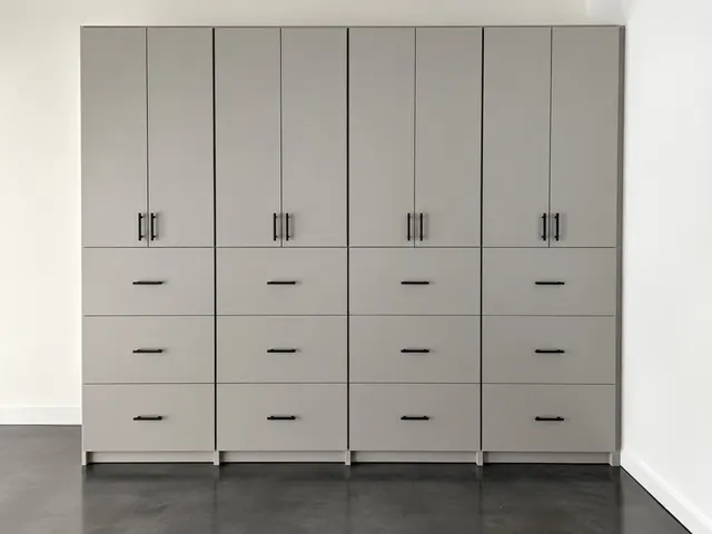 Gray cabinets with black pulls, tall doors over three rows of drawers, on a dark concrete floor