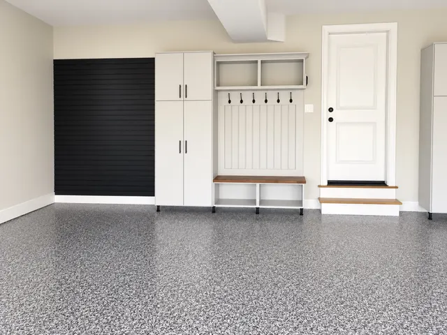 Black slatwall beside a white garage cabinet and a bench with hooks, cubbies and a wood seat
