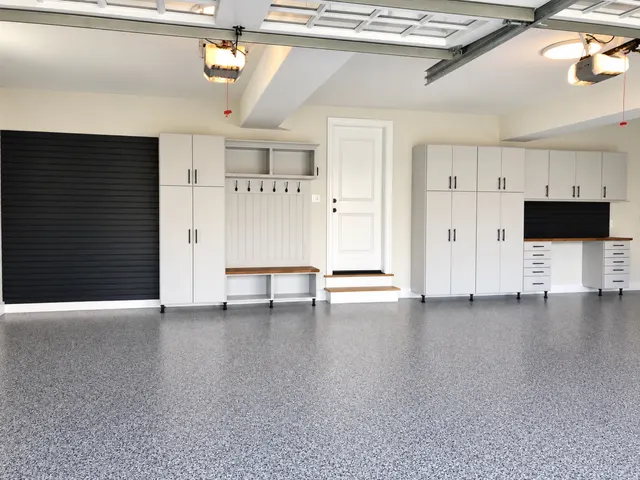 Two-car garage with black slatwall, a bench with hooks, tall cabinets and a workbench on a speckled epoxy floor