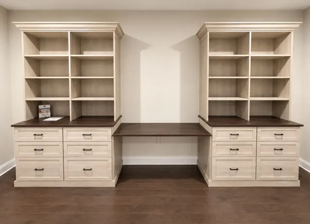 Two light wood bookcases over drawer bases with a dark wood desk spanning between them