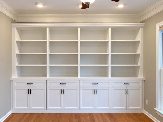White built-in bookcase wall with adjustable shelves over drawers and shaker cabinets with black pulls