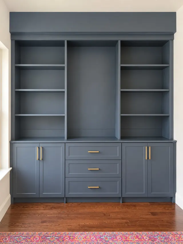 Navy built-in bookcase with open shelves, a center niche and a base of cabinets and drawers with brass pulls