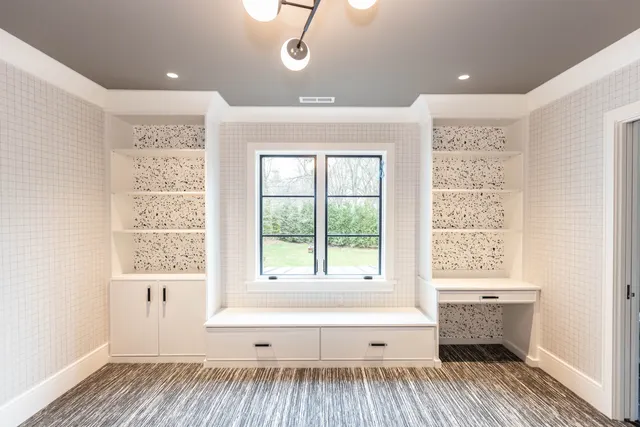 White bookcases with patterned backs flanking a window seat with drawers and a built-in desk