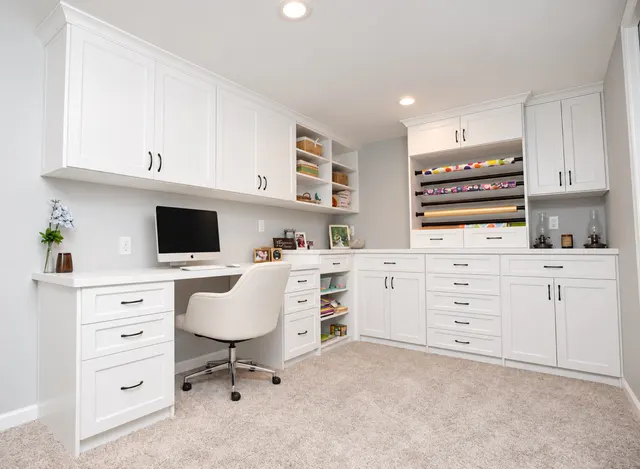 White L-shaped office with a desk and computer, upper cabinets, open shelves, drawers and a wrapping paper rack