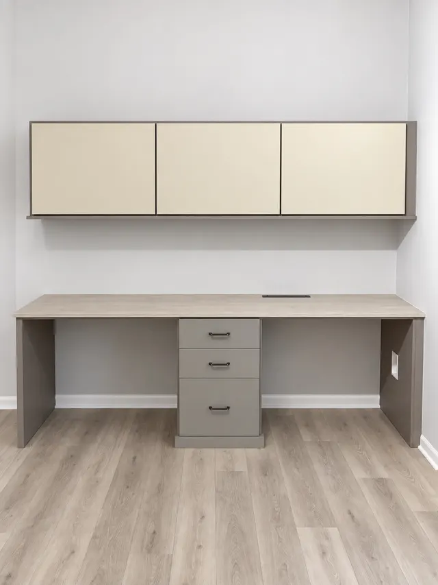 Taupe desk with a light wood top and a three-drawer pedestal under cream wall-hung cabinets