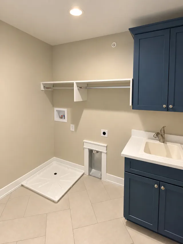 Navy shaker cabinets with a utility sink and white counter beside a white shelf with two hanging rods above washer hookups