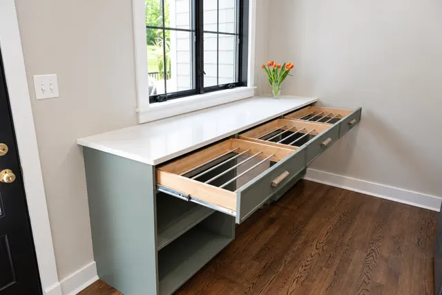 Three pull-out drying rack drawers with metal rods extended from a sage green cabinet under a white counter by a window
