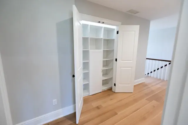 Hallway linen closet with double doors open to white shelving