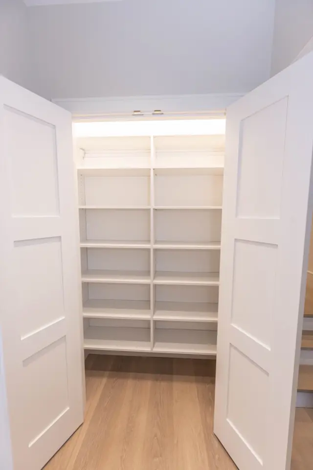 Double-door linen closet with lit white shelving