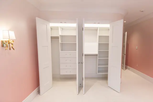 Double-door closets in a pink room with shelving, drawers and hanging