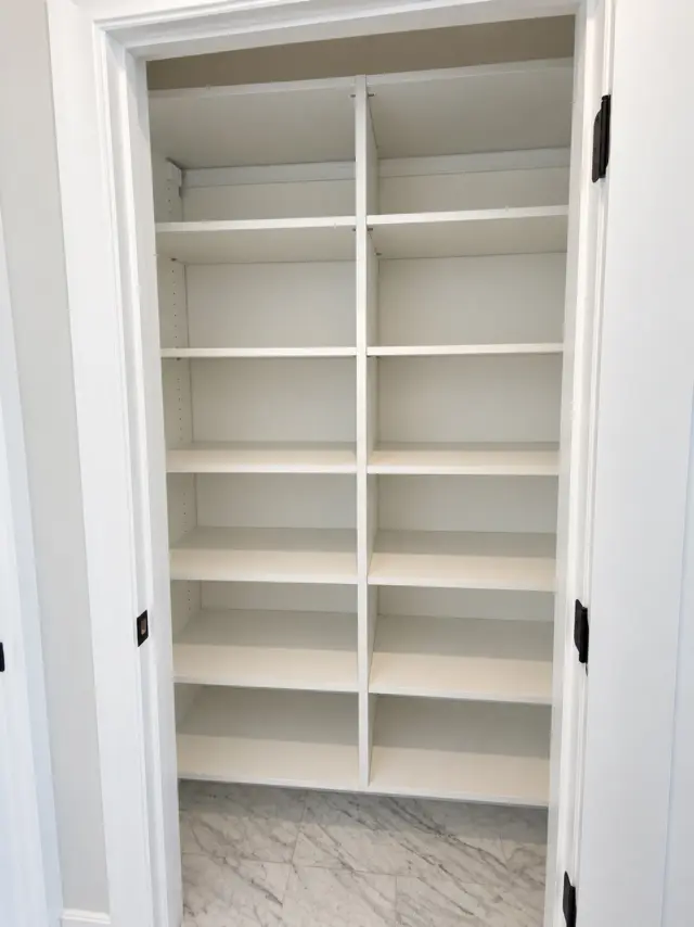 Reach-in closet with two columns of white shelving above a marble floor