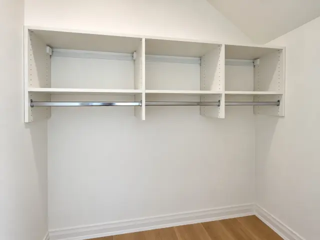 White shelf and hanging rod run across the top of a sloped-ceiling closet
