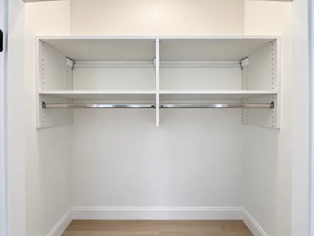 Reach-in closet with a white shelf and chrome hanging rod across its width