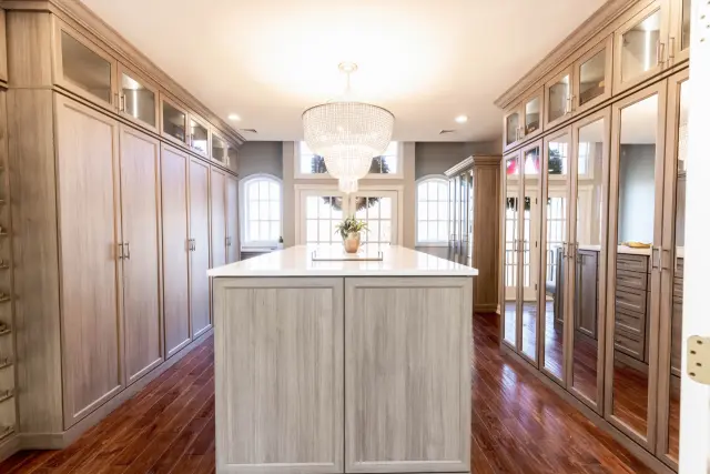 Long walk-in closet with full-height wood-grain cabinets on both walls, a center island and a crystal chandelier