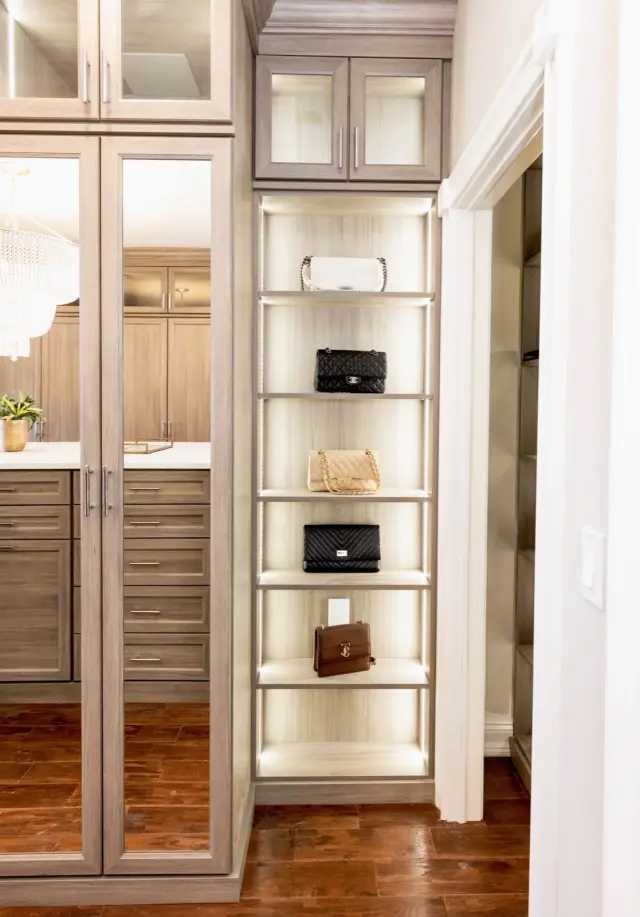 Lit open shelving displaying handbags between wood-grain cabinets