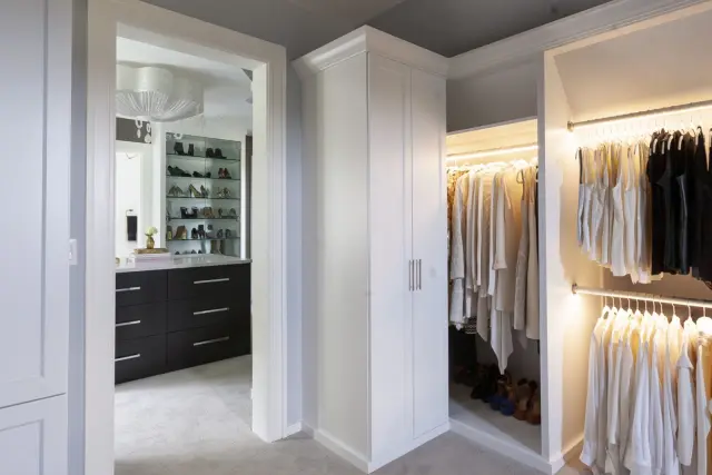 White closet with lit hanging and tall cabinets, seen through the doorway