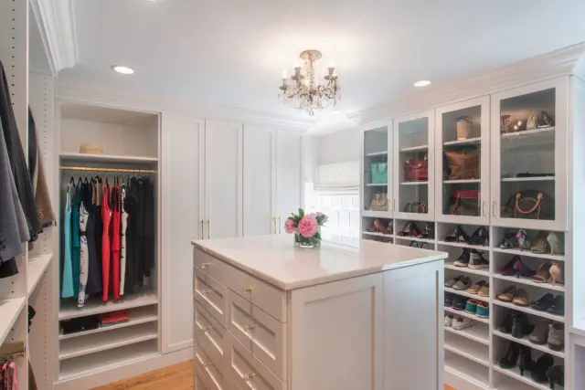 White walk-in closet with a drawer island, glass-front cabinets and shoe shelving