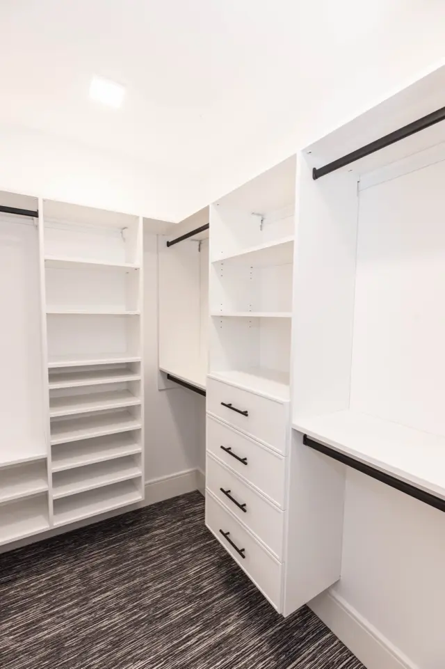 White closet with shoe shelving, drawers and hanging over a patterned carpet