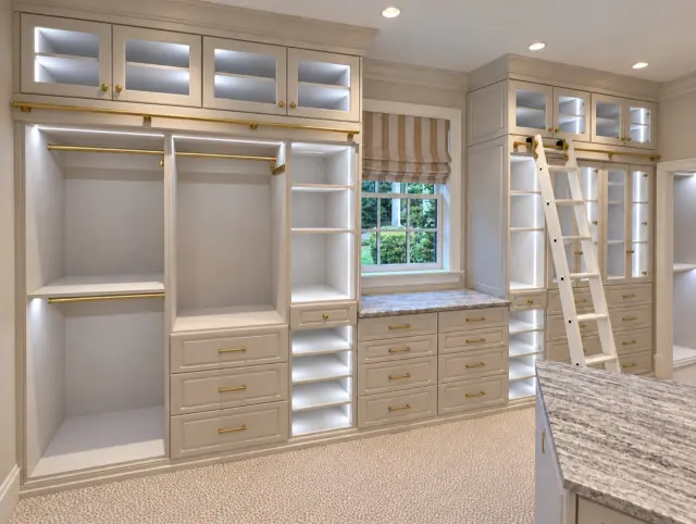 Cream closet with lit glass-front uppers, a window seat and a library ladder