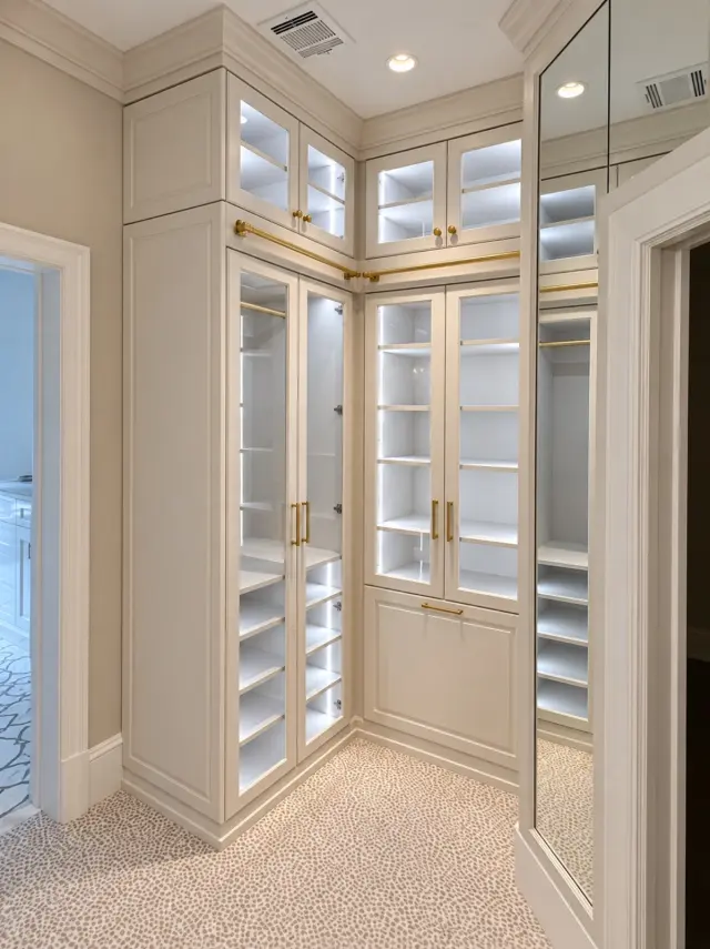 Corner of cream glass-door cabinets with interior lighting and brass handles