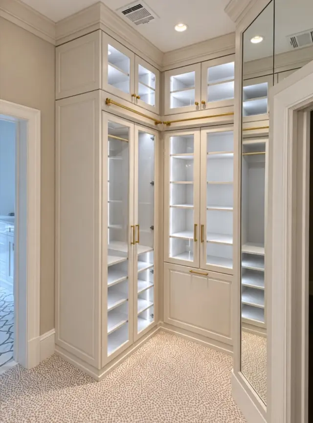 Corner of cream glass-door cabinets with interior lighting beside a mirror