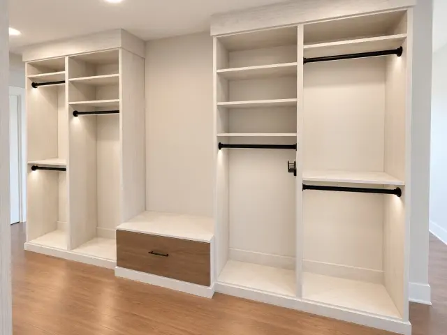 White closet with lit hanging, black rods and a wood-front bench drawer