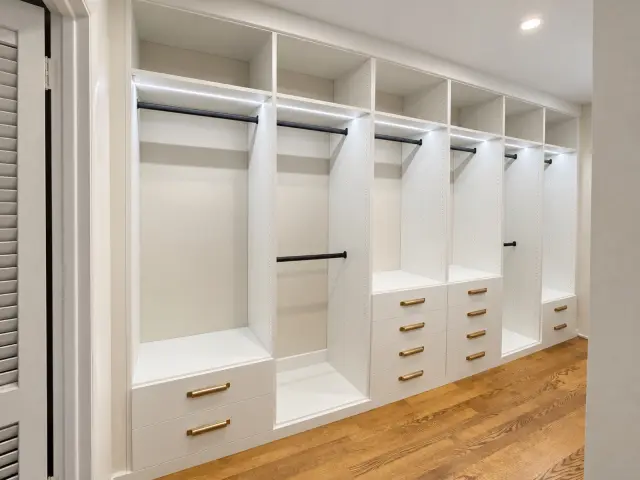 White closet wall with long hanging, black rods and drawer stacks with brass pulls