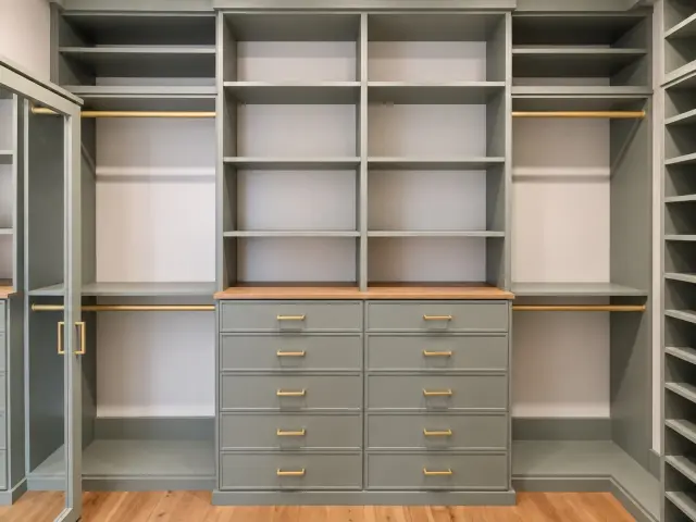 Sage-green closet wall with a drawer bank, wood top and glass doors