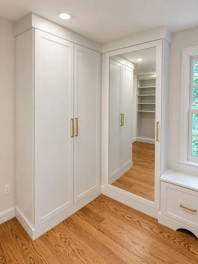 White tall cabinets beside a full-length mirror and window