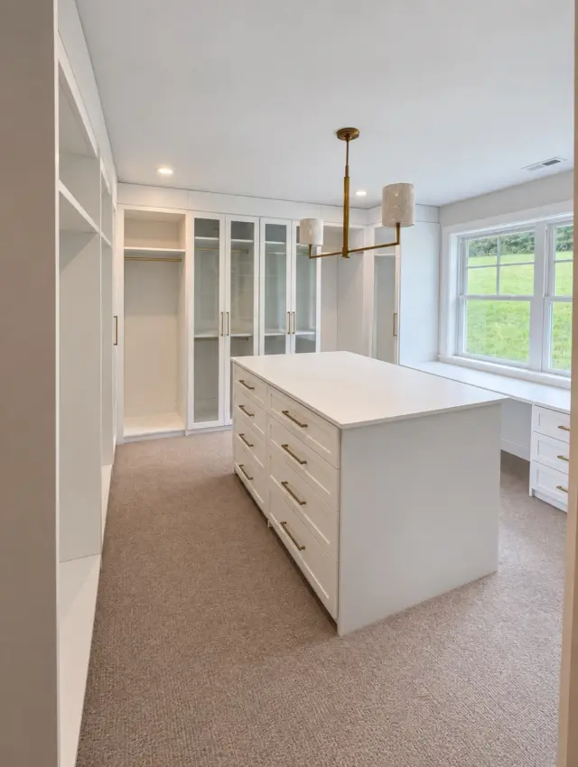 White walk-in closet with a drawer island, glass-door cabinets and a pendant light
