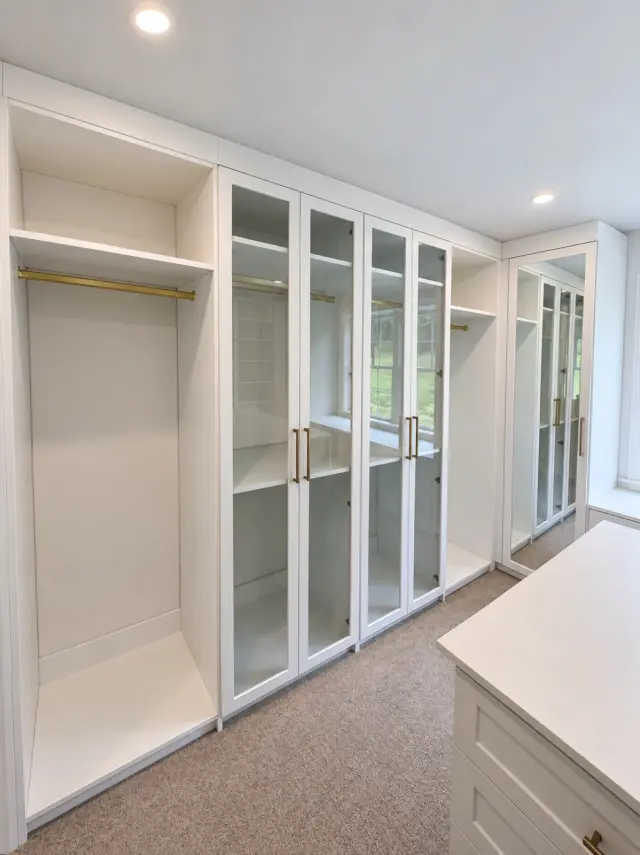 White closet with glass-door cabinets and open hanging