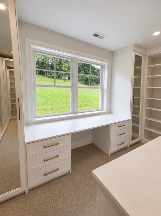 White built-in desk with drawers beneath a window, between shelving