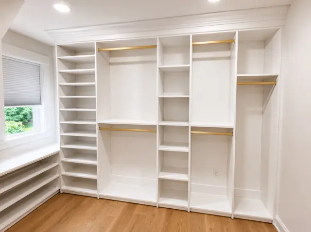White closet with shelving, brass rods and a low shelf under a window