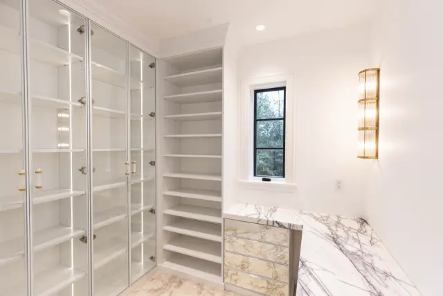 Bright closet with glass-door cabinets, open shelving and a marble-top vanity