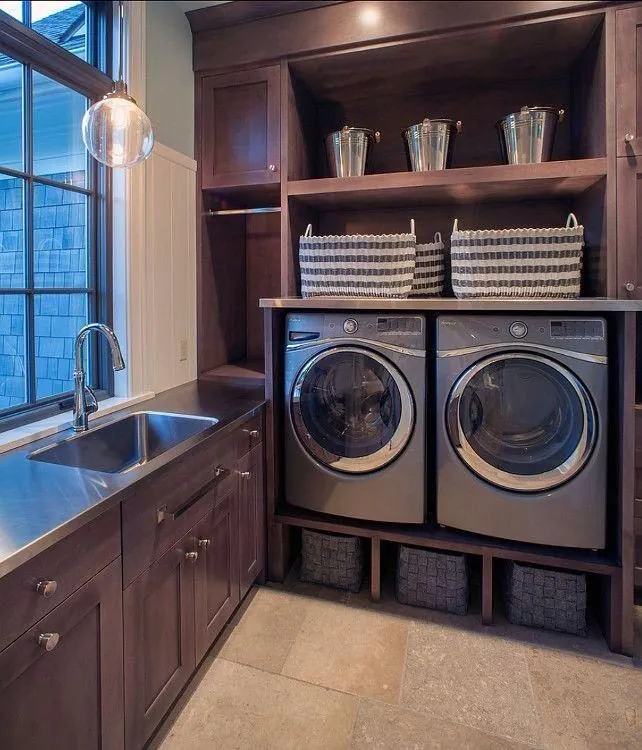 Dark wood laundry cabinets with a sink and a front-load washer and dryer on a pedestal
