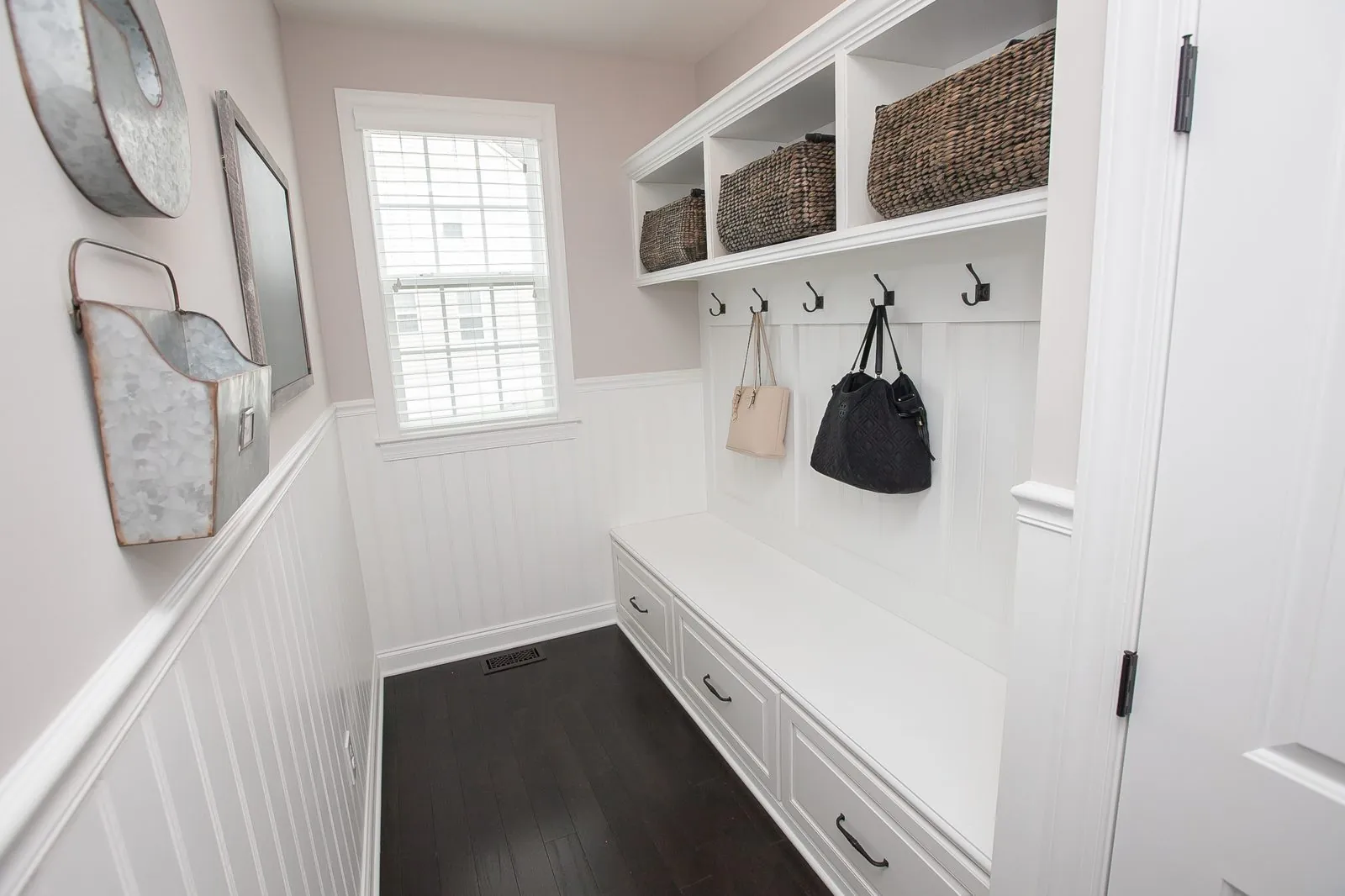 White mudroom bench with hooks and upper cubbies with baskets