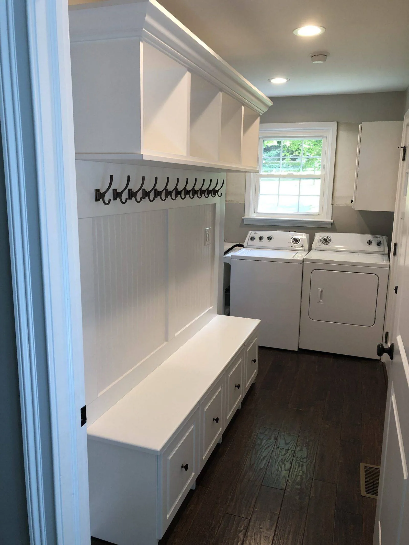 White mudroom bench with hooks beside a washer and dryer