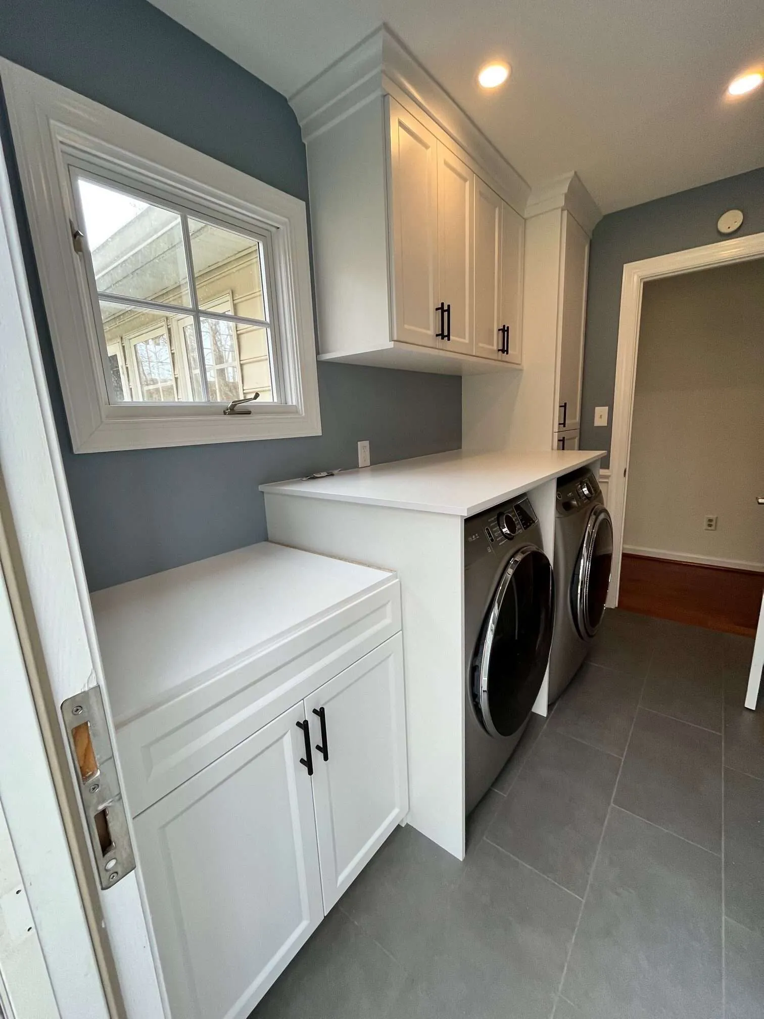 White laundry cabinets beside a front-load washer under a window